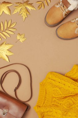 Kahverengi deri kadın çanta, turuncu örme kazak, sıcak çizmeler, kahverengi arka plan üst görünüm düz altın sonbahar yaprağı yatıyordu. Modaya uygun kadın aksesuarları. Sonbahar Moda Konsepti. Şık Bayan Giyim