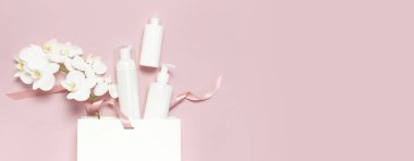 Düz beyaz kozmetik şişe kapları hediye çantası pembe arka plan üst görünümünde Beyaz Phalaenopsis orkide çiçekler yatıyordu. Kozmetik Spa markalama mock-up Doğal organik güzellik ürünü kavramı Minimalizm tarzı