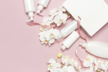 Düz beyaz kozmetik şişe kapları hediye çantası pembe arka plan üst görünümünde Beyaz Phalaenopsis orkide çiçekler yatıyordu. Kozmetik Spa markalama mock-up Doğal organik güzellik ürünü kavramı Minimalizm tarzı