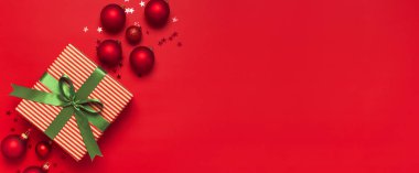 Noel arkaplanı. Yeşil kurdeleli hediye, kırmızı Noel topları, kırmızı arka plan manzaralı konfeti şeklinde yıldızlar. Yeni yıl hediyeleri: Flat Lay Xmas bayramı 2020