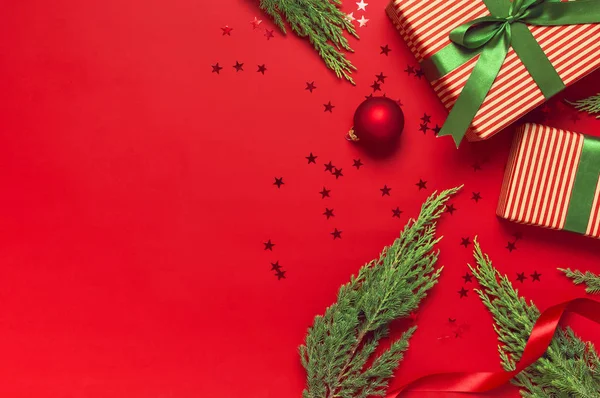 Fundo de Natal. Presente com fita verde, bolas vermelhas, ramos de árvore de natal, estrelas de confete na vista superior de fundo vermelho. Ano Novo apresenta decorações festivas Flat lay Natal feriado 2020 celebratio — Fotografia de Stock