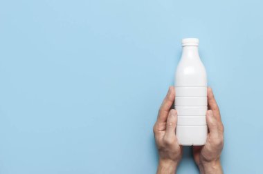 Süt ürünleri için beyaz plastik şişeler erkeklerin elinde mavi arka plan manzaralı düz yerde. Plastik Kefir Yoğurt Şişe Sütü. Paketleme şablonu modeli. Tasarımınız için düzenName