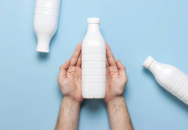 Süt ürünleri için beyaz plastik şişeler erkeklerin elinde mavi arka plan manzaralı düz yerde. Plastik Kefir Yoğurt Şişe Sütü. Paketleme şablonu modeli. Tasarımınız için düzenName