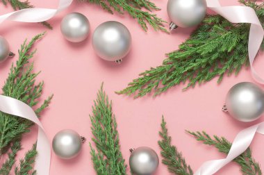 Gümüş Noel oyuncak topları, tatil kurdeleleri, pembe arka planda noel ağacı dalları. Düz görünüm kopyalama alanı yatıyordu. Yeni yıl kompozisyonu, kış dekorasyonu. En az kutlama konsepti