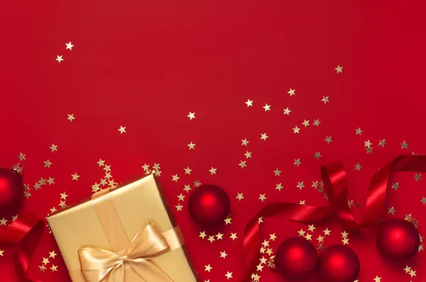 Appartement vacances Noël 2020 célébration. Nouvel An cadeaux d'or de Noël avec ruban, boules de Noël, étoiles de confettis d'or sur fond rouge vue de dessus. Coffrets cadeaux carte de vœux Décorations festives — Photo