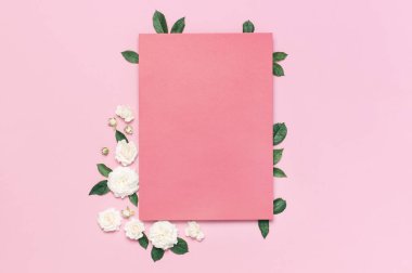 Çiçek kompozisyonu. Pembe boş kağıt, beyaz taze gül ve yumuşak pembe arka plan üzerinde yeşil yaprakları. Düz döşeme, üst görünüm, kopyalama alanı. Çiçek kartı, selamlama, tatil maketleri. Sevgililer Günü arka plan