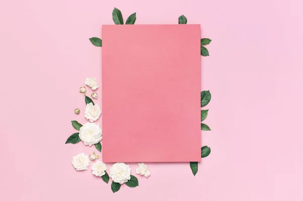 Composição de flores. Papel em branco rosa, rosas brancas frescas e folhas verdes no fundo rosa doce. Deitado plano, vista superior, espaço de cópia. Cartão de flores, saudação, maquete de férias. Dia dos Namorados fundo — Fotografia de Stock