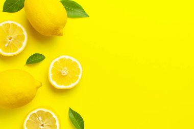 Taze limonlar ve parlak sarı arka planda yeşil yapraklarla yaratıcı bir altyapı. Üst görünüm düz kopya alanı. Limonlu turunçgiller minimum C vitamini bileşimi, limon dilimleriyle.