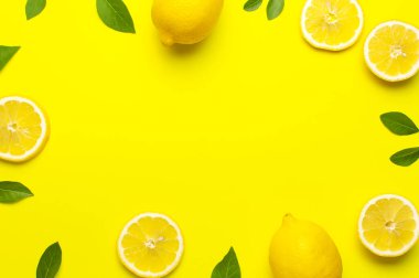 Taze limonlar ve parlak sarı arka planda yeşil yapraklarla yaratıcı bir altyapı. Üst görünüm düz kopya alanı. Limonlu turunçgiller minimum C vitamini bileşimi, limon dilimleriyle.