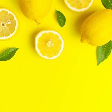 Taze limonlar ve parlak sarı arka planda yeşil yapraklarla yaratıcı bir altyapı. Üst görünüm düz kopya alanı. Limonlu turunçgiller minimum C vitamini bileşimi, limon dilimleriyle.
