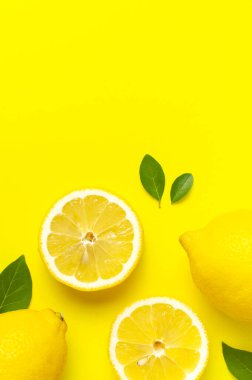 Taze limonlar ve parlak sarı arka planda yeşil yapraklarla yaratıcı bir altyapı. Üst görünüm düz kopya alanı. Limonlu turunçgiller minimum C vitamini bileşimi, limon dilimleriyle.