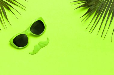 Yaratıcı parti dekorasyonu konsepti. Yeşil bıyık, güneş gözlüğü, fotoğraf kabinleri için aksesuar, yeşil arka planda palmiye yaprakları düz görünüm fotokopi alanı. Babalar Günü, Erkekler Sağlık Bilinci Ayı