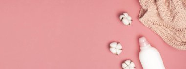 Çevre temizliği konsepti. Çamaşır deterjanı beyaz plastik ambalajı, sıvı tozu, çamaşır deterjanı, yün kazak, pembe arka planda pamuk çiçekleri. Düz manzaralı. Biyo organik ürün