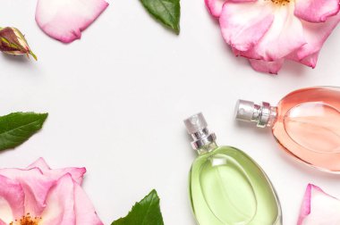 Parfüm ve çiçeklerle güzel bir kompozisyon. Parfüm şişesi, gül çiçekleri açık arkaplan manzaralı yeşil yapraklar düz kopya alanı yatıyordu. Kozmetik parfümü tuvalet suyu parfümü koleksiyonu.