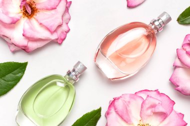 Parfüm ve çiçeklerle güzel bir kompozisyon. Parfüm şişesi, gül çiçekleri açık arkaplan manzaralı yeşil yapraklar düz kopya alanı yatıyordu. Kozmetik parfümü tuvalet suyu parfümü koleksiyonu.