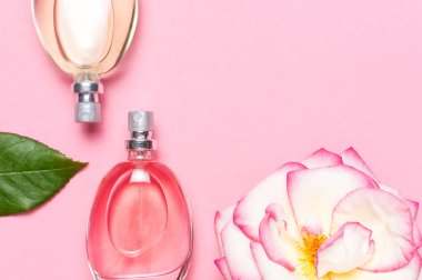 Parfüm ve çiçeklerle güzel bir kompozisyon. Parfüm şişeleri, gül çiçekleri... Pembe arka planda yeşil yapraklar... Kozmetik parfümü tuvalet suyu parfümü koleksiyonu.