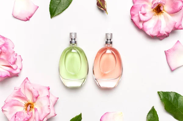 Beautiful composition with perfume and flowers. Perfume bottle, rose flowers petals green leaves on light background top view Flat lay copy space. Perfumery cosmetics toilet water fragrance collection.