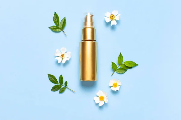 Cosmetic mock up gold bottles. Cosmetics, spring white flowers green leaves on blue background. Cosmetics springtime summer Concept. Flat lay top view copy space. Branding products, beauty background.
