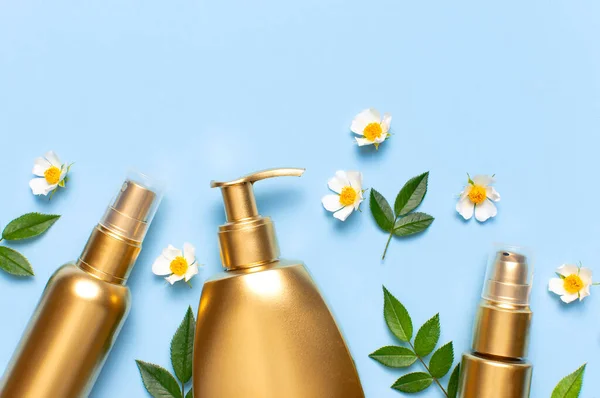 Cosmetic mock up gold bottles. Cosmetics, spring white flowers green leaves on blue background. Cosmetics springtime summer Concept. Flat lay top view copy space. Branding products, beauty background.