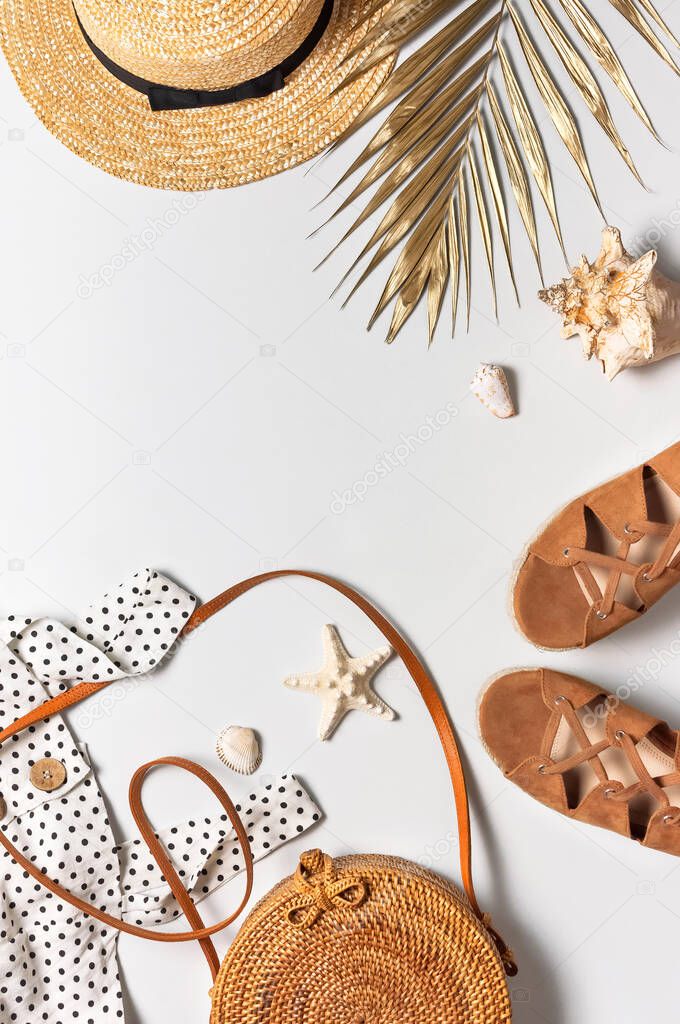 Summer women's white dress in black peas rattan woven bag brown sandals straw hat golden palm leaf shells starfish on light background. Flat lay top view. Women's beach fashion, travel vacation.