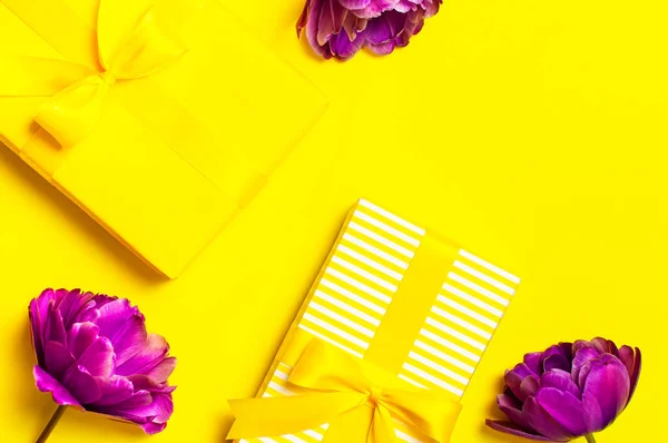 Bright yellow gift present box with ribbon and purple tulips on yellow background top view. Flat lay holiday background. Birthday present, March 8, Mother\'s Day, Valentine\'s Day. Congratulation.