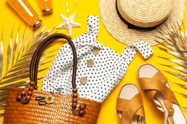 Yaz arkaplanı plaj aksesuarları. Plaj hasır hasır hasır örgü kadın eko çanta beyaz elbise şapka altın tropikal yaprak suyu cam kavanozlarda saman kabukları sarı arka planda deniz yıldızı. Düz üst görünüm