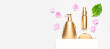Kozmetik, altın şişelerini taklit ediyor. Kozmetik ürünleri, beyaz hediye çantası, arka planda pembe ortanca çiçekleri. Kozmetik ilkbahar yaz konsepti. Düz manzaralı. Marka ürünleri, kaplıca, güzellik geçmişi.