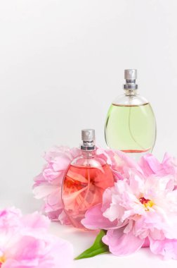 Parfüm ve çiçeklerle güzel bir kompozisyon. Parfüm şişesi, pembe çiçekler şakayıklar açık arkaplanda yeşil yapraklar düz bir kopya alanı uzanıyor parfüm kozmetik tuvalet suyu parfümü koleksiyonu.