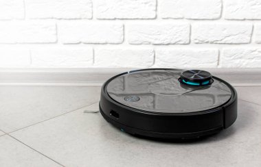 Ev Temizliği Konsepti. Modern robot elektrikli süpürge, tuğla duvara karşı porselen fayanslardaki evleri temizliyor. Yeni teknolojiler, hızlı ev temizleme otomatik robot asistanı. Temizlik için akıllı aygıt.