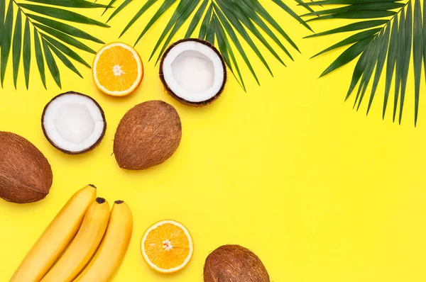 Summer tropical composition. Frame of Green tropical leaves of palm trees, coconut, orange, bananas on bright yellow background. Flat lay, top view, copy space. Creative background food, fruit