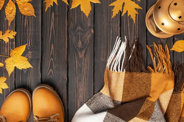 秋天时尚的概念。棕色橙色皮靴，皮靴上有毛皮，格子的温暖格子花，金秋叶，装饰金灯在棕色木制背景的顶部视图。时髦的女鞋 — 图库照片