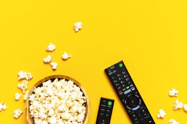 Siyah TV, ses uzaktan kumandası ve parlak sarı arka planda patlamış mısır. Uzaktan kumandalı minimal arkaplan, bir film, dizi, set-top kutular, ses sistemi.