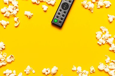 Siyah TV uzaktan kumandası ve parlak sarı zemin üzerinde patlamış mısır üst görünüm kopyalama alanı yatıyordu. Uzaktan kumandalı minimal arkaplan, bir film, dizi, set-top kutular, ses sistemi.