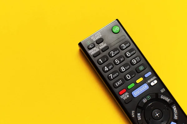 Black TV remote control on bright yellow background flat lay top view copy space. Minimalistic background with a remote control, watching TV, set-top boxes, audio system, soundbar.