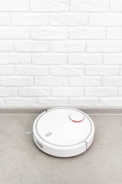 Ev Temizliği Konsepti. Modern robot elektrikli süpürge, tuğla duvara karşı porselen fayanslardaki evleri temizliyor. Yeni teknolojiler, hızlı ev temizleme otomatik robot asistanı. Temizlik için akıllı aygıt.