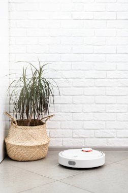 Ev Temizliği Konsepti. Modern robot elektrikli süpürge, tuğla duvara karşı porselen fayanslardaki evleri temizliyor. Yeni teknolojiler, hızlı ev temizleme otomatik robot asistanı. Temizlik için akıllı aygıt.