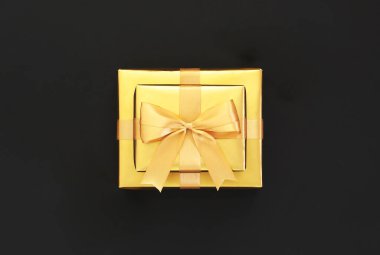 Siyah arka planda kurdeleli altın bir hediye. Düz konum, üst görünüm, kopyalama alanı. Altın madalyalar, parti, doğum günü, tatil konsepti. Hediye kutusu, sürpriz. Yeni Yıl veya Noel kompozisyonu.