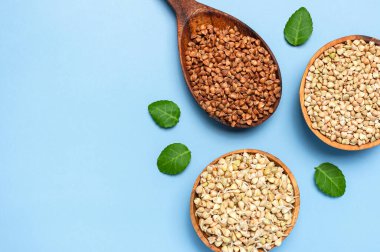 Yeşil karabuğday, ahşap kaselerde filizlenen karabuğday kahverengi karabuğday taneleri ahşap kaşıkta ve mavi arka planda yeşil yapraklar. Düz manzaralı. Sağlıklı vejetaryen gıda eko ürünleri diyet organik hasat.