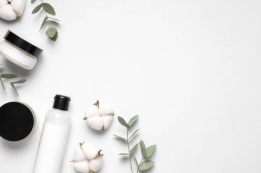 Doğal organik kozmetik ürünleri. Güzellik uzmanının markalı maketi. Krem ve losyonlu kozmetik kaplar, pamuk çiçekleri, okaliptüs yaprakları gri arka planda düz manzarada yatıyordu. Damgalamak için boş etiket.