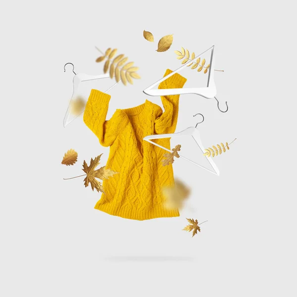Suéter de punto amarillo naranja para mujer voladora Perchas de madera blancas hojas doradas de otoño sobre fondo gris. Venta de otoño Concepto de ropa creativa moda otoño invierno acogedor jersey jersey. Moda femenina — Foto de Stock