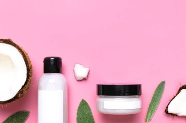 Hindistan cevizi yağlı doğal organik kozmetik ürünleri. Krem ve losyonlu kozmetik kaplar, kırık hindistan cevizi, pembe arka planda yeşil yapraklar düz manzarada yatıyordu. Güzellik uzmanının markalı maketi. Boş etiket.