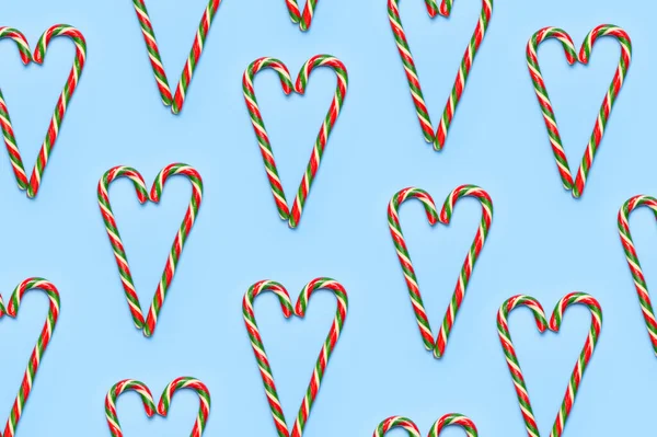 Tradycyjne świąteczne cukierki trzciny cukrowej, lizak w kształcie serca na niebieskim tle płaski leżał widok z góry. Kreatywna noworoczna koncepcja żywności. Uroczysty wystrój, słodycz, karmelowe cukierki. Symbol świąt Bożego Narodzenia — Zdjęcie stockowe
