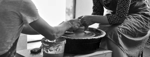 Black and white A man teaches a girl to make clay products on a potter\'s wheel. Hands in clay.