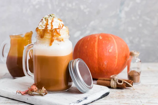 Spicy pumpkin latte with spices and a cap of whipped cream decorated with salted caramel and crushed pumpkin seeds