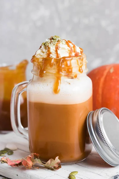 Spicy pumpkin latte with spices and a cap of whipped cream decorated with salted caramel and crushed pumpkin seeds