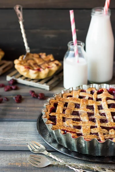 Traditional American cherry pie and mini pies on a dark wooden background