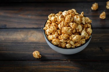 Tuzlu karamelli patlamış mısır, beyaz tabakta, siyah ahşap arka planda.