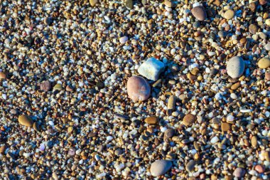 sahil arka plan taşları üzerinde deniz çakıl renkli granit. Kum ve çakıl taşlarıyla sahilin kıyısı deniz dalgalarıyla yıkanmış..