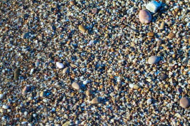 sahil arka plan taşları üzerinde deniz çakıl renkli granit. Kum ve çakıl taşlarıyla sahilin kıyısı deniz dalgalarıyla yıkanmış..