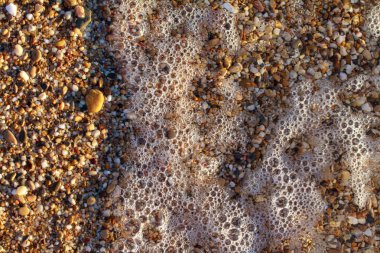 sahil arka plan taşları üzerinde deniz çakıl renkli granit. Kum ve çakıl taşlarıyla sahilin kıyısı deniz dalgalarıyla yıkanmış..